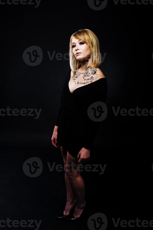 Studio portrait of blonde girl with originally make up on neck, wear on black dress at dark background. photo