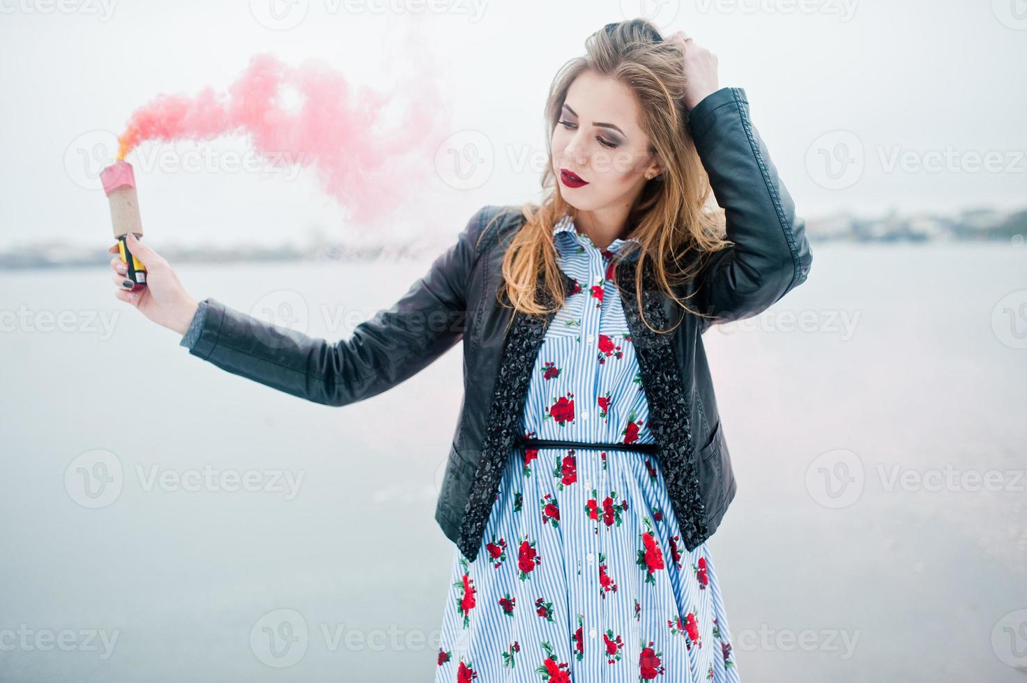 Stylish girl in leather jacket hold pink smoke flare at winter day against frozen lake. photo