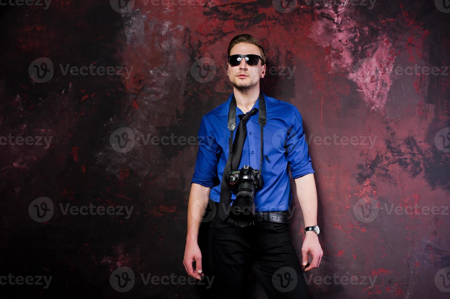 Studio portrait of stylish professional photographer man with camera, wear on blue shirt and necktie, sunglasses. photo