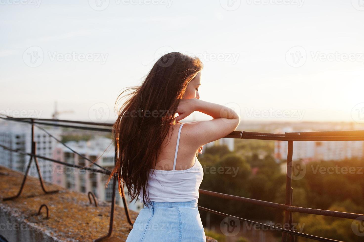 Portrait of a gorgeous young woman in casual clothing admiring the sunset from the roof of a building. photo