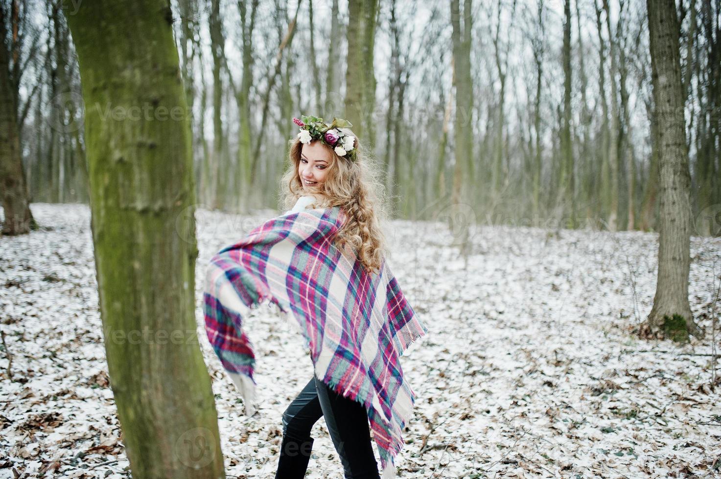 Curly cute blonde girl with wreath in checkered plaid at snowy forest in winter day. photo