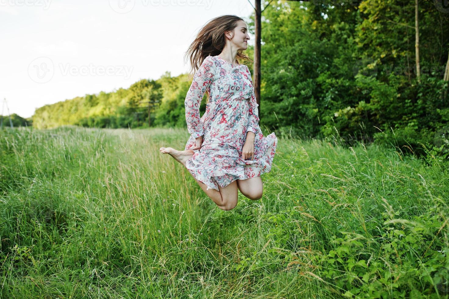 Portrait of a stunning young girl in dress jumping on the meadow. photo