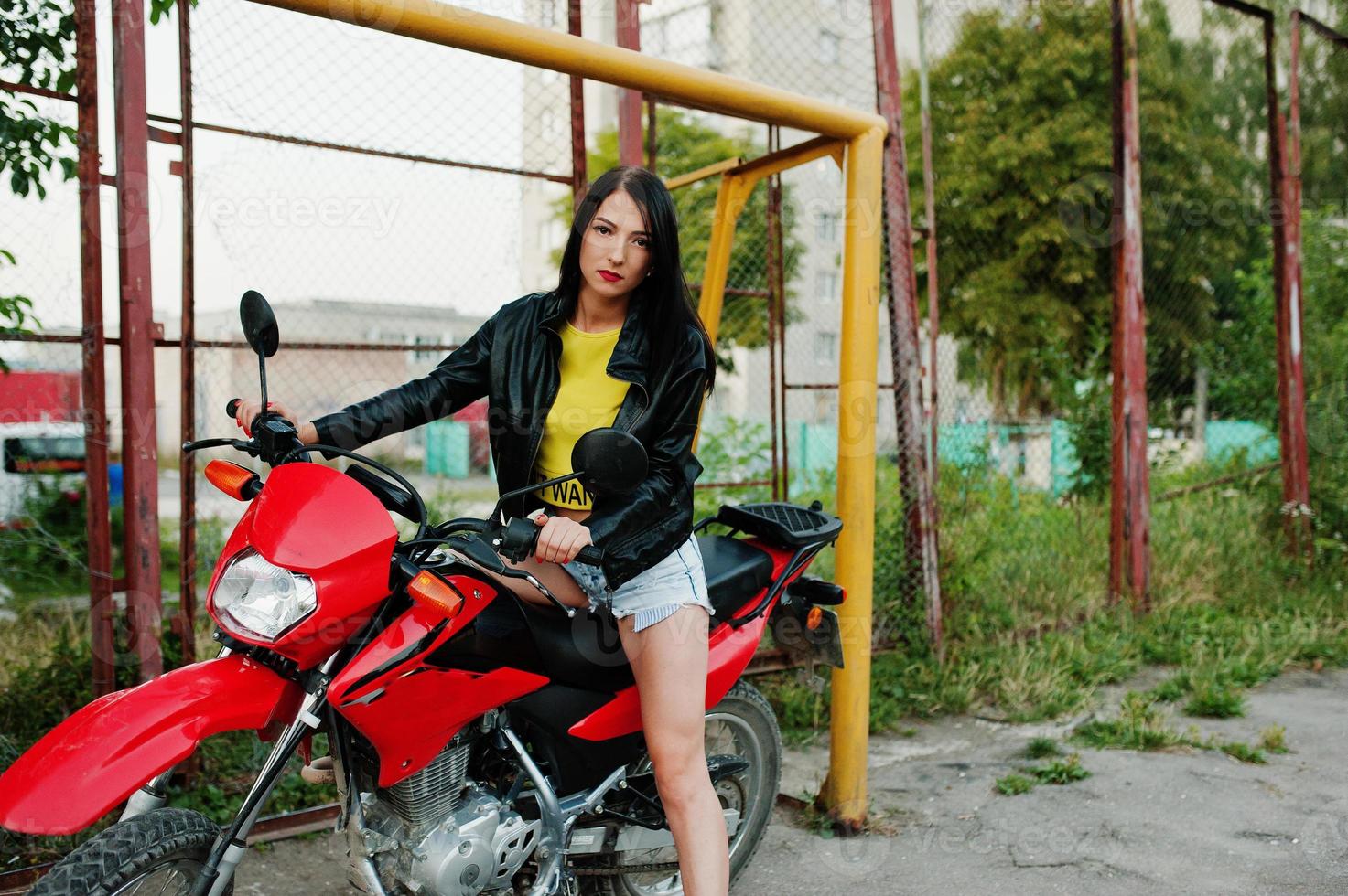 Portrait of a cool and awesome woman in dress and black leather jacket sitting on a cool red motorbike. photo