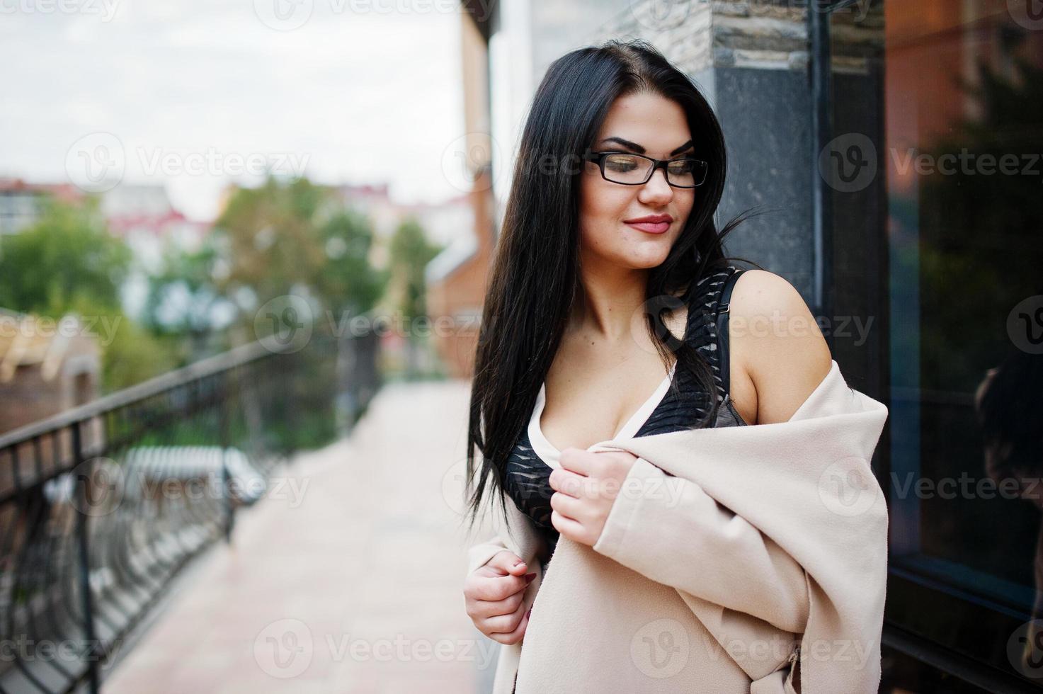 mujer sexy de pelo negro con gafas y posado contra un edificio con ventanas modernas. Foto de stock Vecteezy