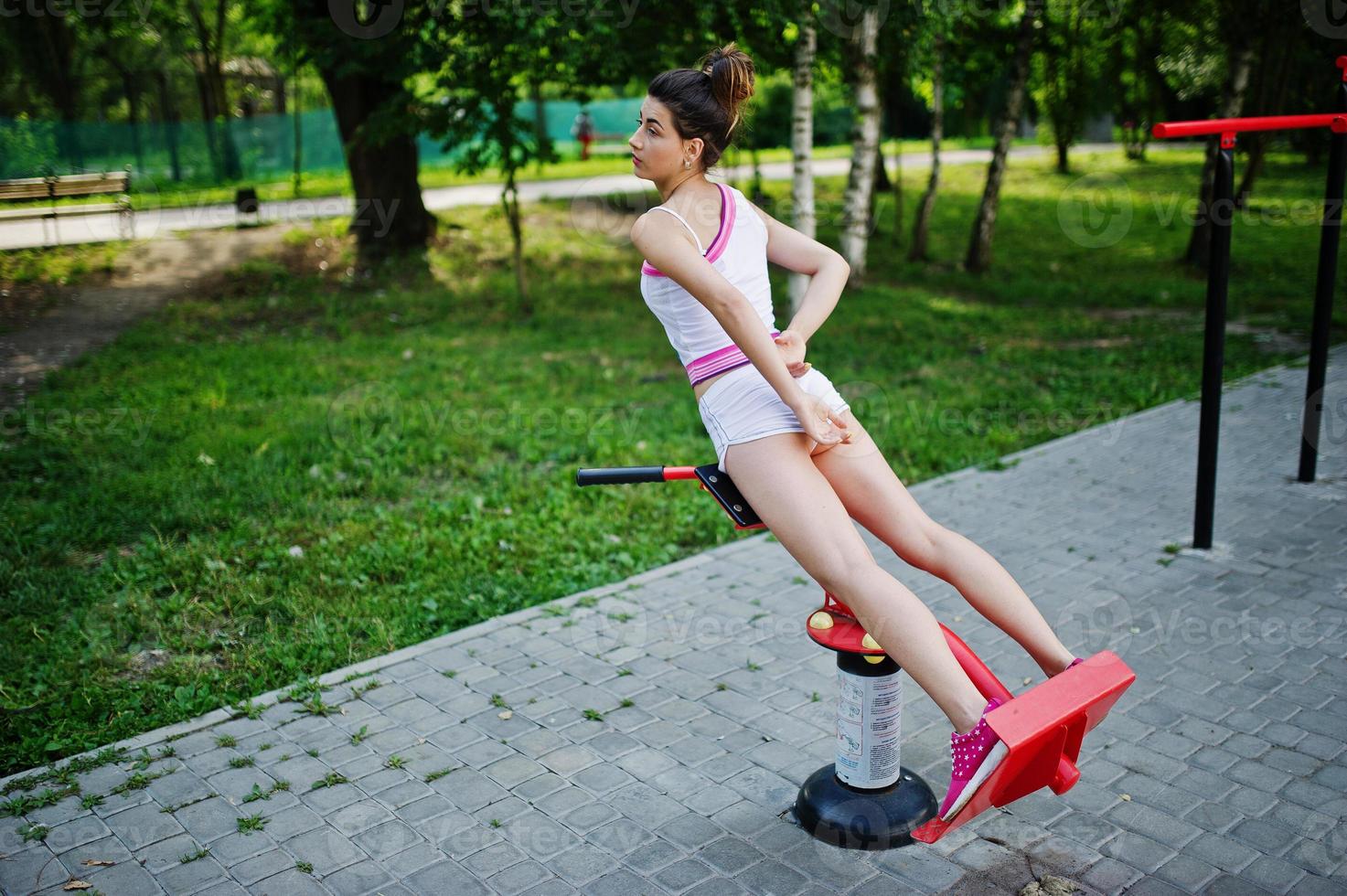 Sport girl wear on white shorts ans shirt doing exercises on simulators outdoor at park. photo