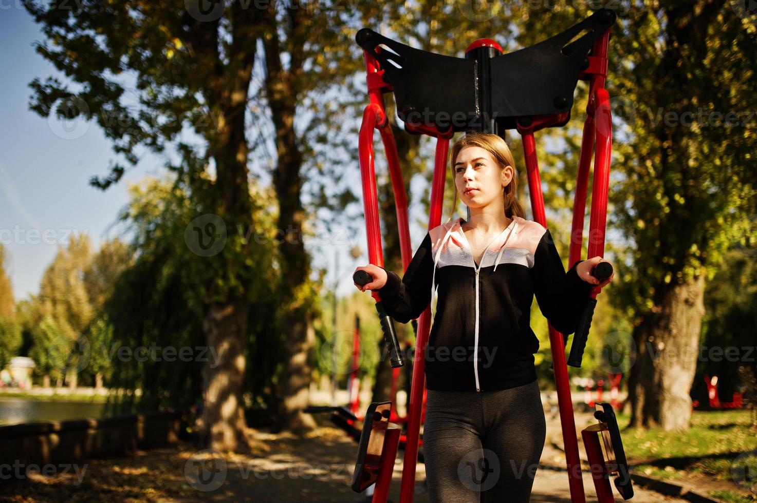 Young girl has the training and doing exercise outdoors on street simulators. Sport, fitness, street workout concept. photo