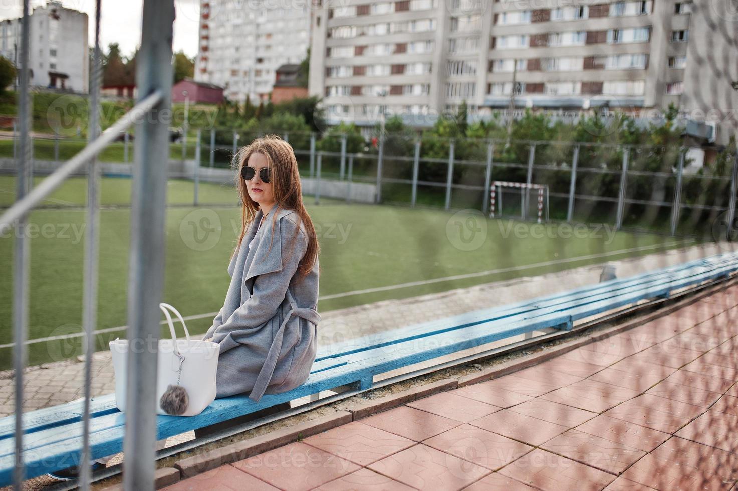 Girl in gray coat with sunglasses at small street stadium. photo