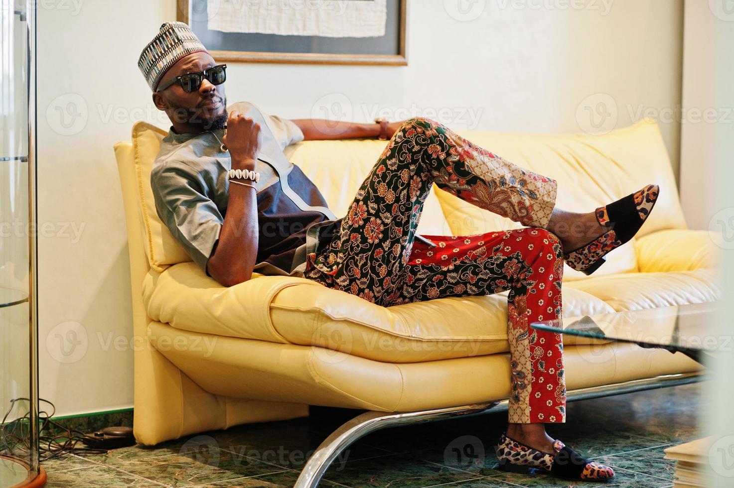 Rich african man sitting on sofa at his appartment. Portrait of successful black man indoor. photo