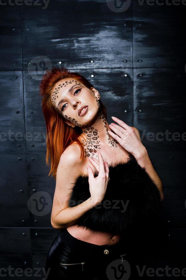 Fashion model red haired girl with originally make up like leopard predator against steel wall. Studio portrait. photo