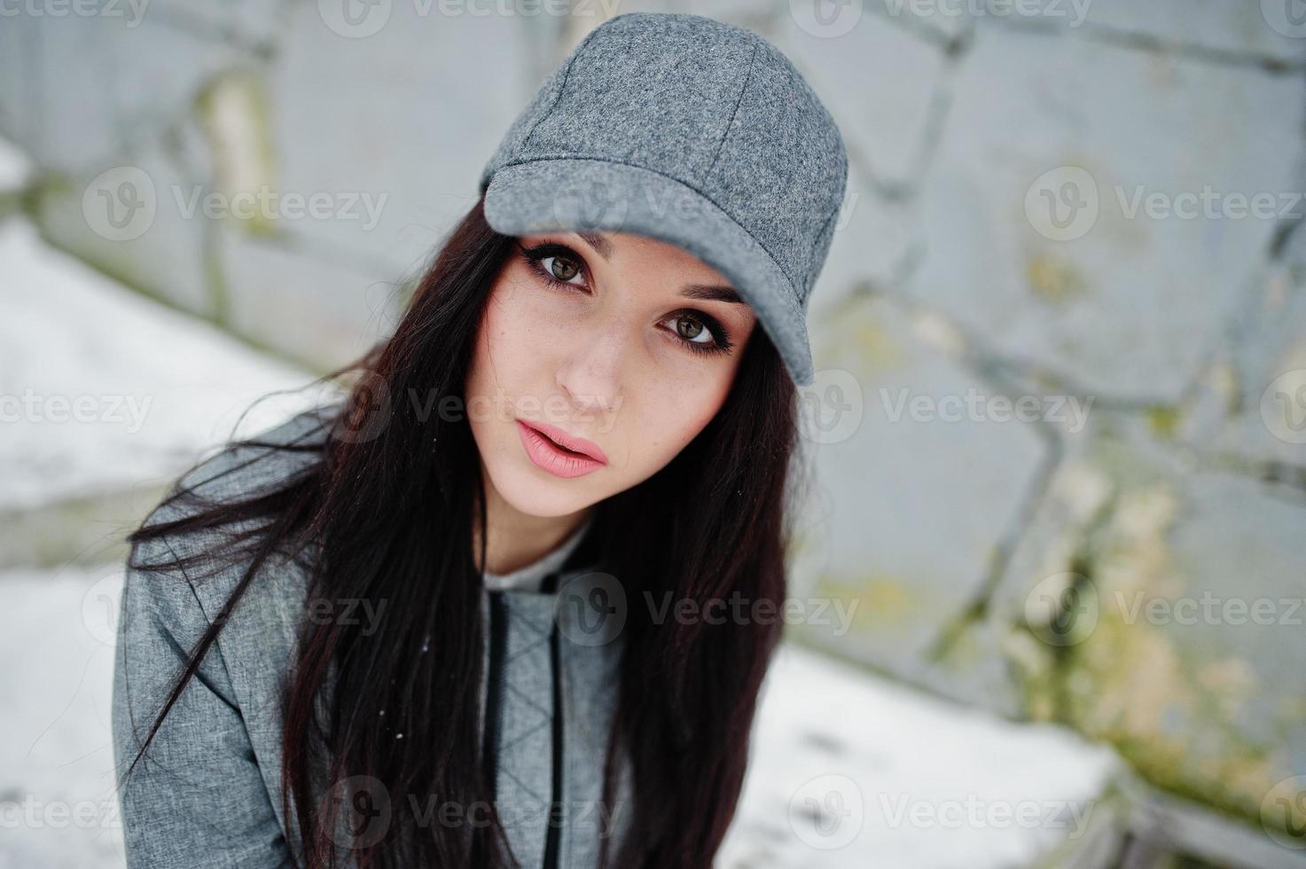 Stylish brunette girl in gray cap, casual street style on winter day against colored wall. photo