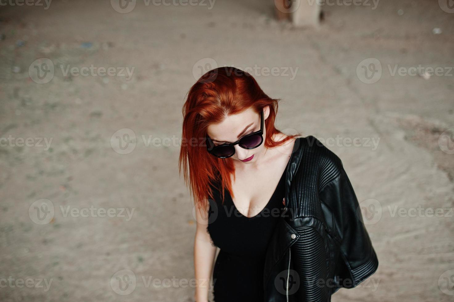 Red haired stylish girl in sunglasses wear in black, against abadoned place. photo