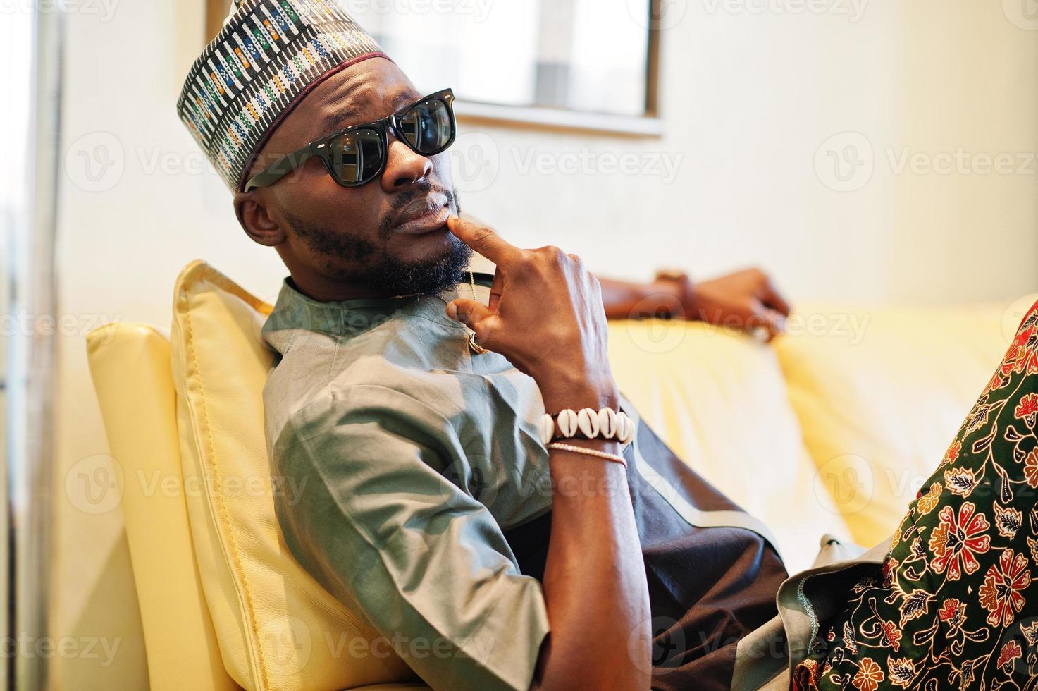 Rich african man sitting on sofa at his appartment. Portrait of successful black man indoor. photo