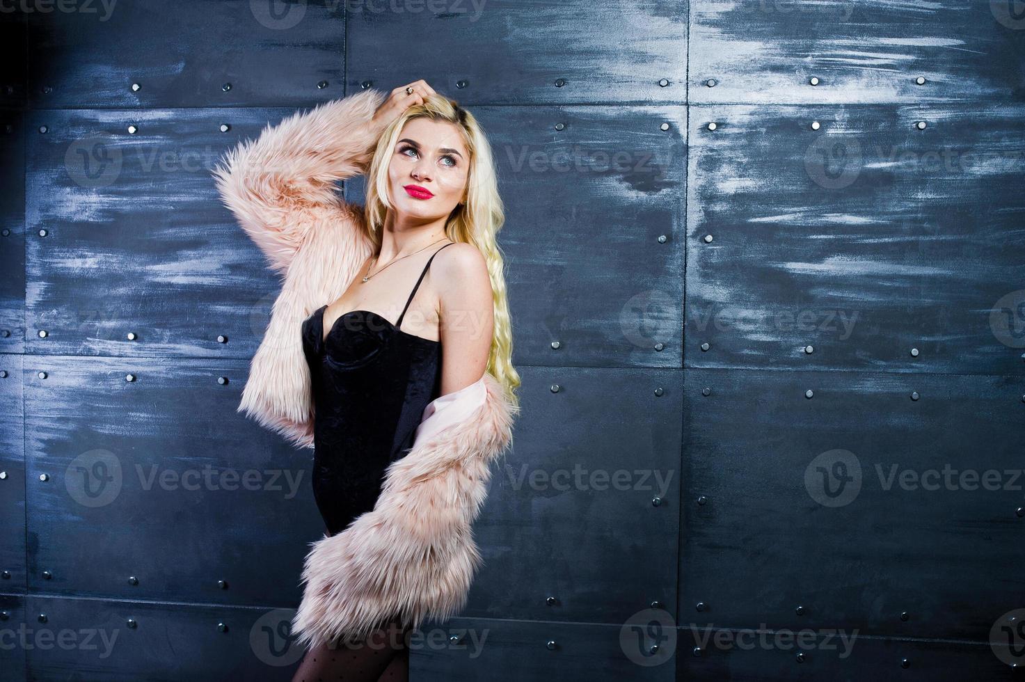 Elegante blonde girl wear on fur coat and combi dress posed against steel wall on studio. photo