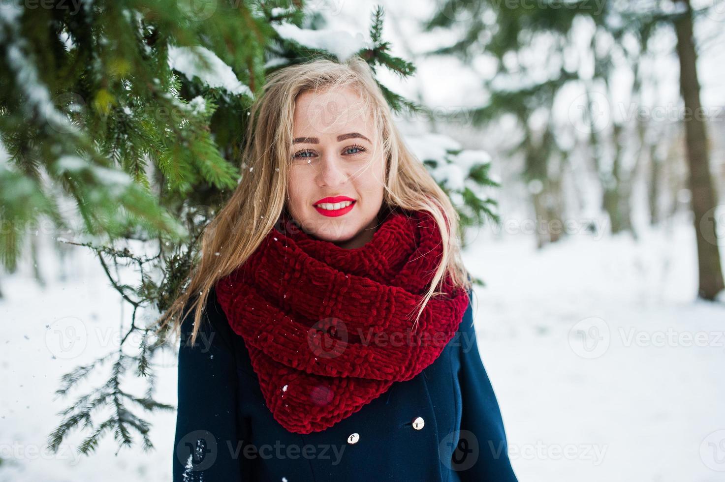 Blonde girl in red scarf and coat walking at park on winter day. photo