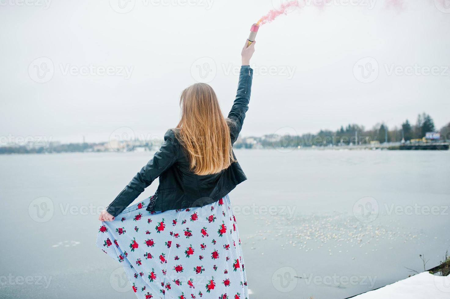 Stylish girl in leather jacket hold pink smoke flare at winter day against frozen lake. photo