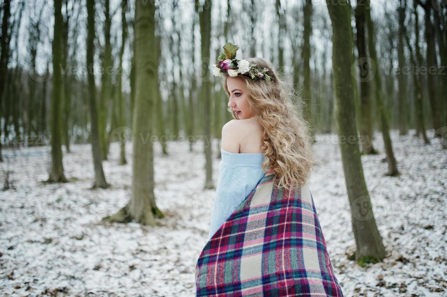 Curly cute blonde girl with wreath in checkered plaid at snowy forest in winter day. photo