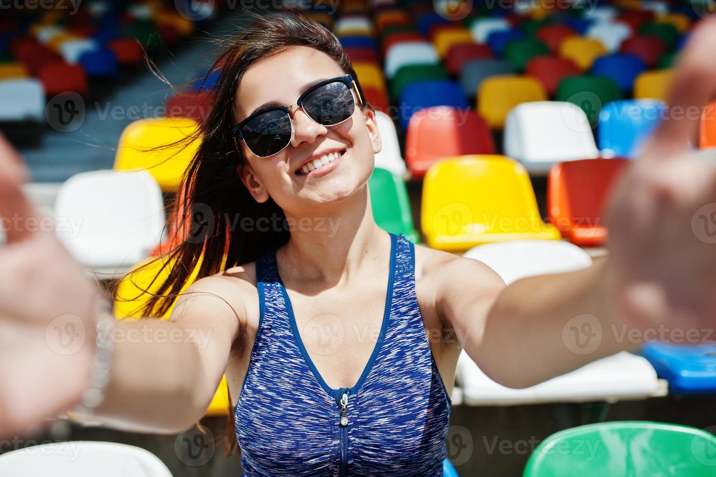 retrato de primer plano de una hermosa chica en forma con gafas de sol sentada en el estadio. foto