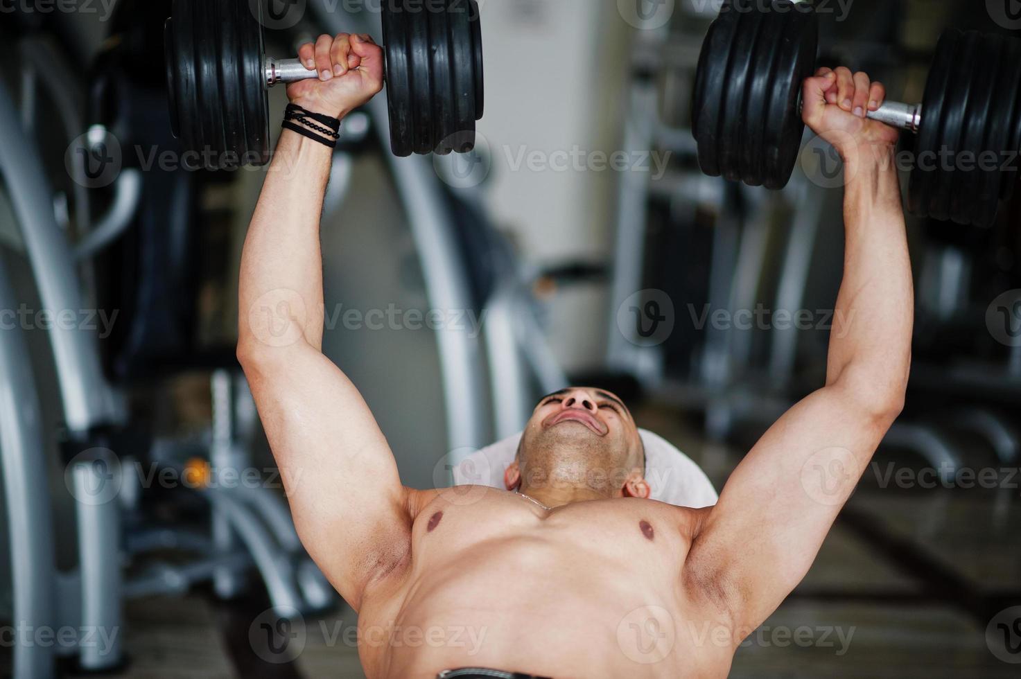 hombre árabe musculoso entrenando con pesas gimnasio moderno. hombres árabes fitness con el torso desnudo haciendo ejercicio. foto