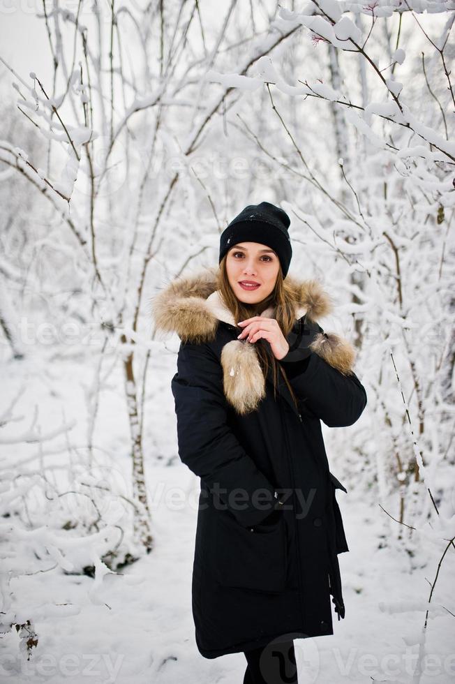 Beautiful brunette girl in winter warm clothing. Model on winter jacket and black hat. photo