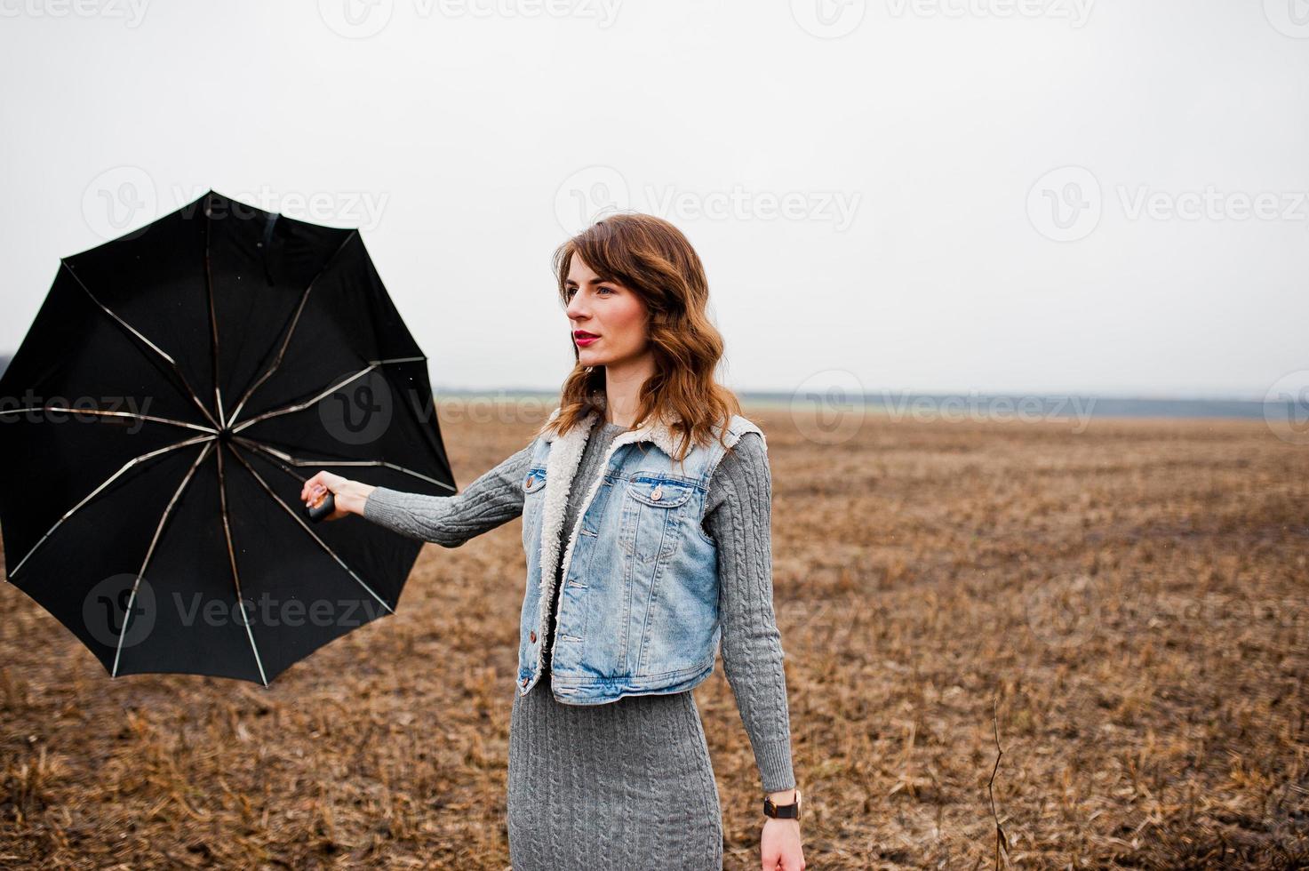 Portrait of brunette curly girl in jeans jacket with black umbrella at field. photo