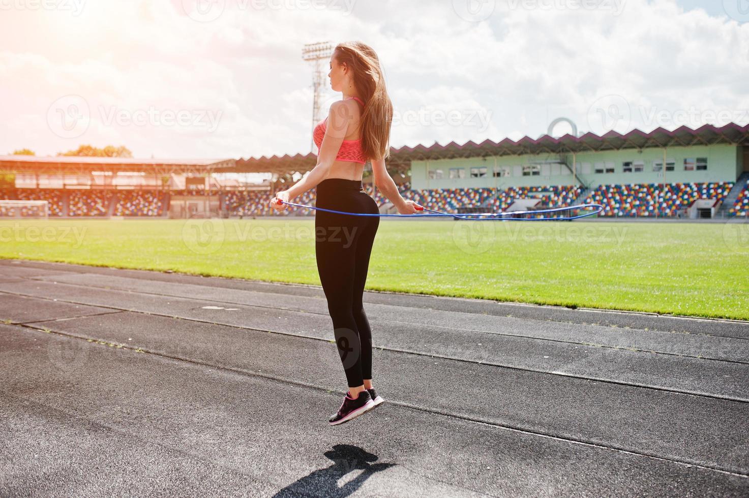 Fitness sporty girl in sportswear at a football stadium outdoor sports. Happy sexy woman workout and jumping with rope. photo