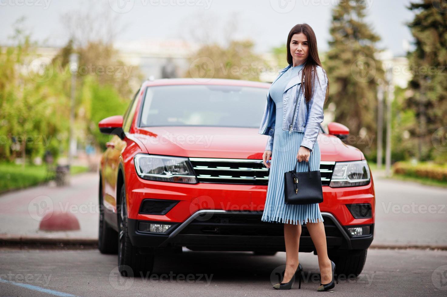 Outdoor photo of gorgeous woman with handbag posing near orange suv car.