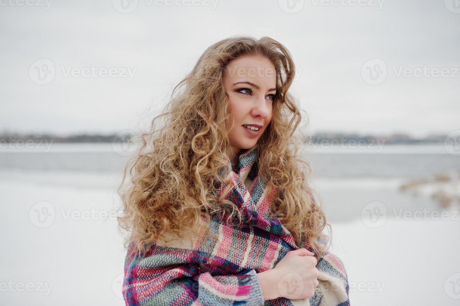 Curly blonde girl in checkered plaid against frozen lake at winter day. photo