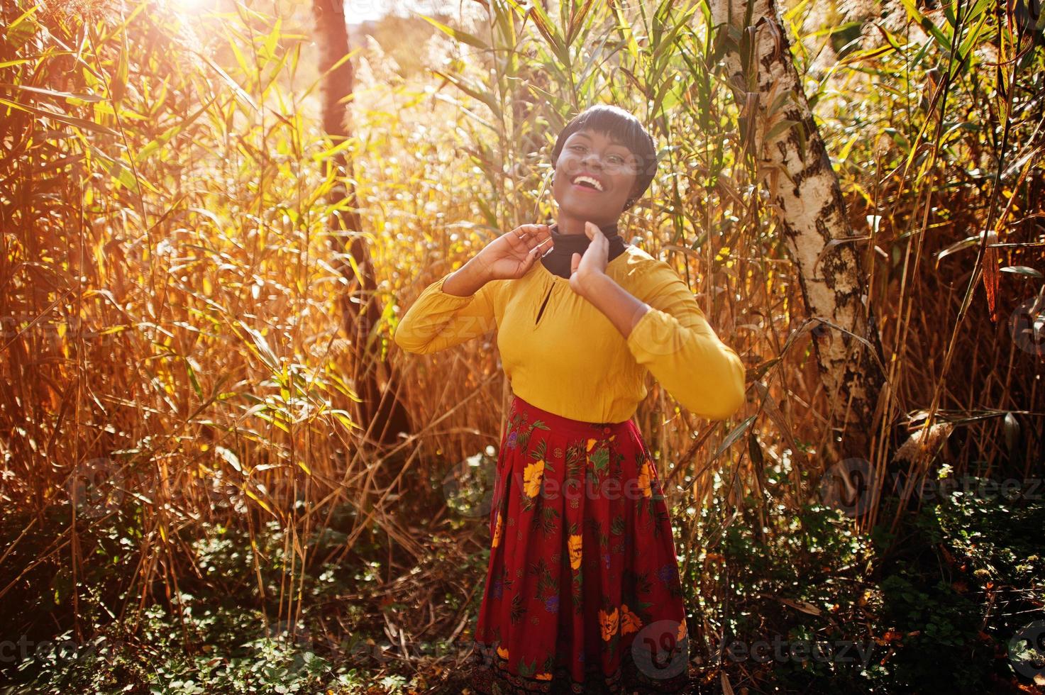 niña afroamericana con vestido amarillo y rojo en el parque de otoño dorado. foto