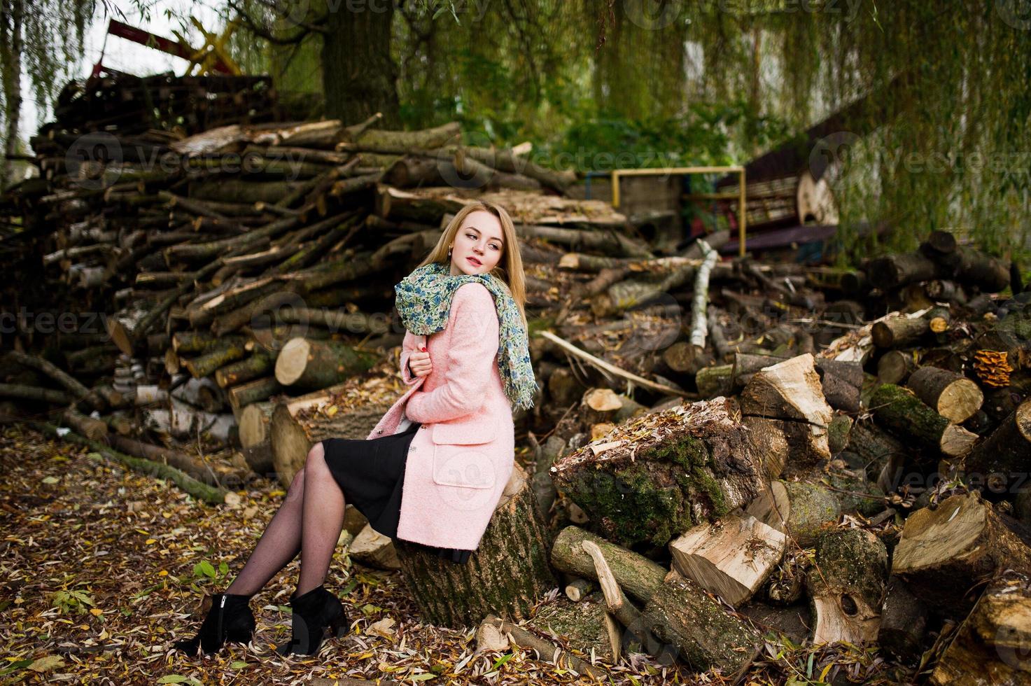 joven rubia con abrigo rosa posada sobre fondo de tocones de madera. foto