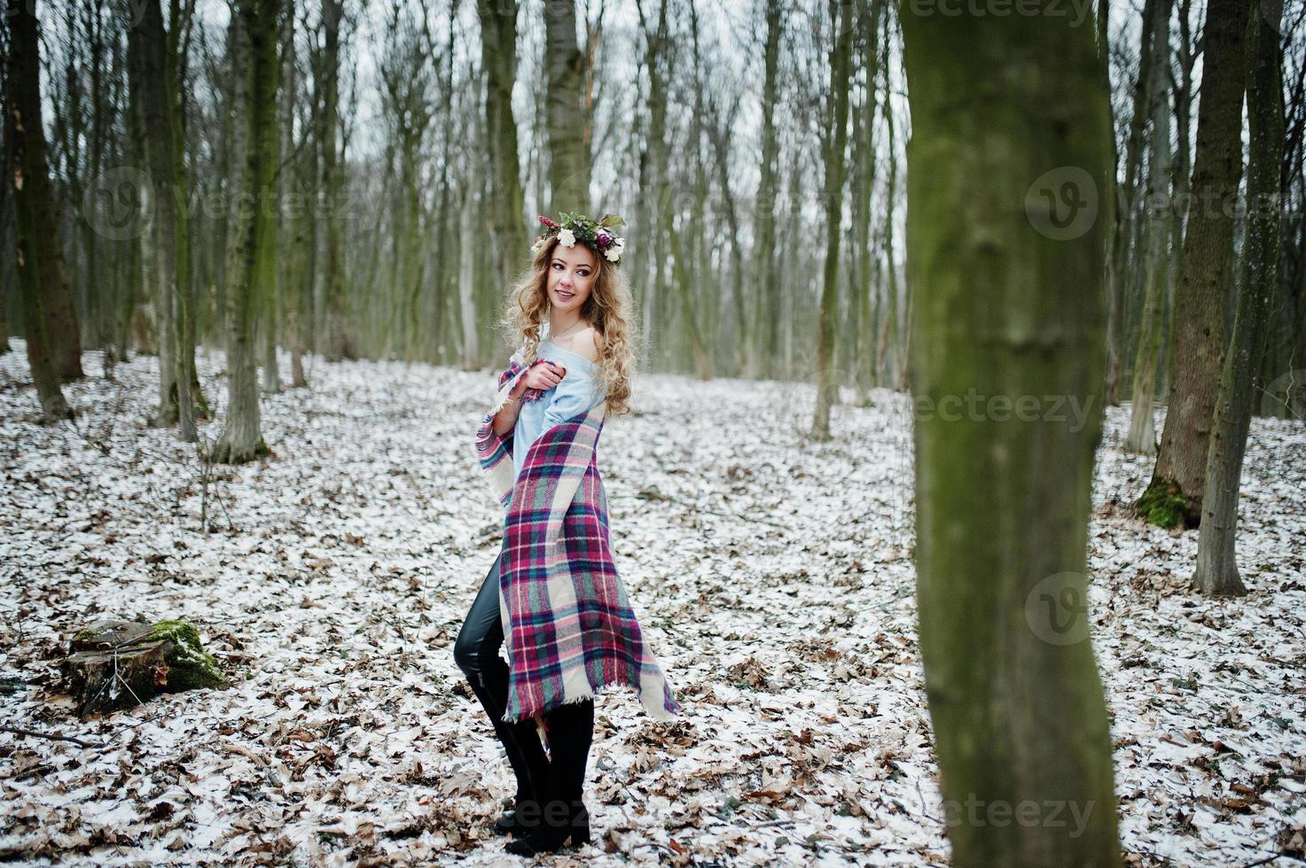 Curly cute blonde girl with wreath in checkered plaid at snowy forest in winter day. photo