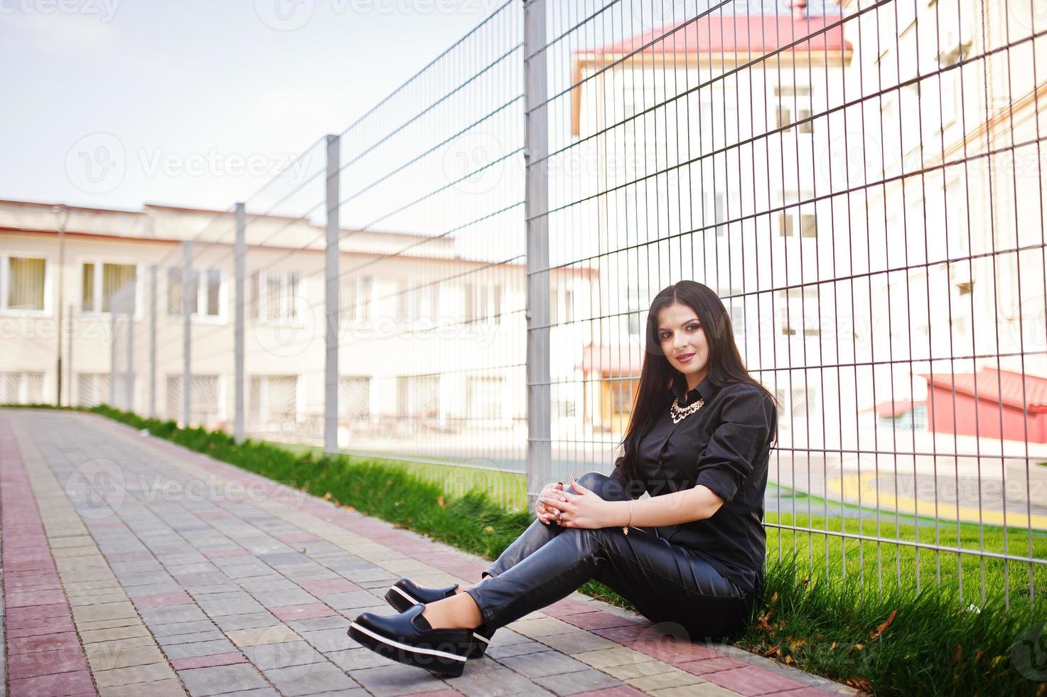 Fashion outdoor photo of gorgeous sensual woman with dark hair in elegant clothes sitting against iron fence at autumn city.