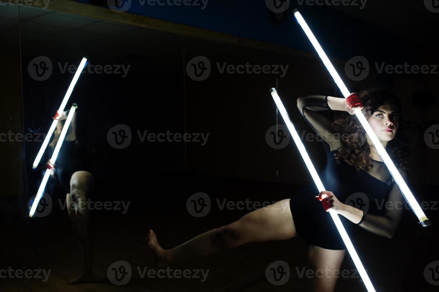 Curly brunette plus size model with two long led lamp at dance room with mirror. photo