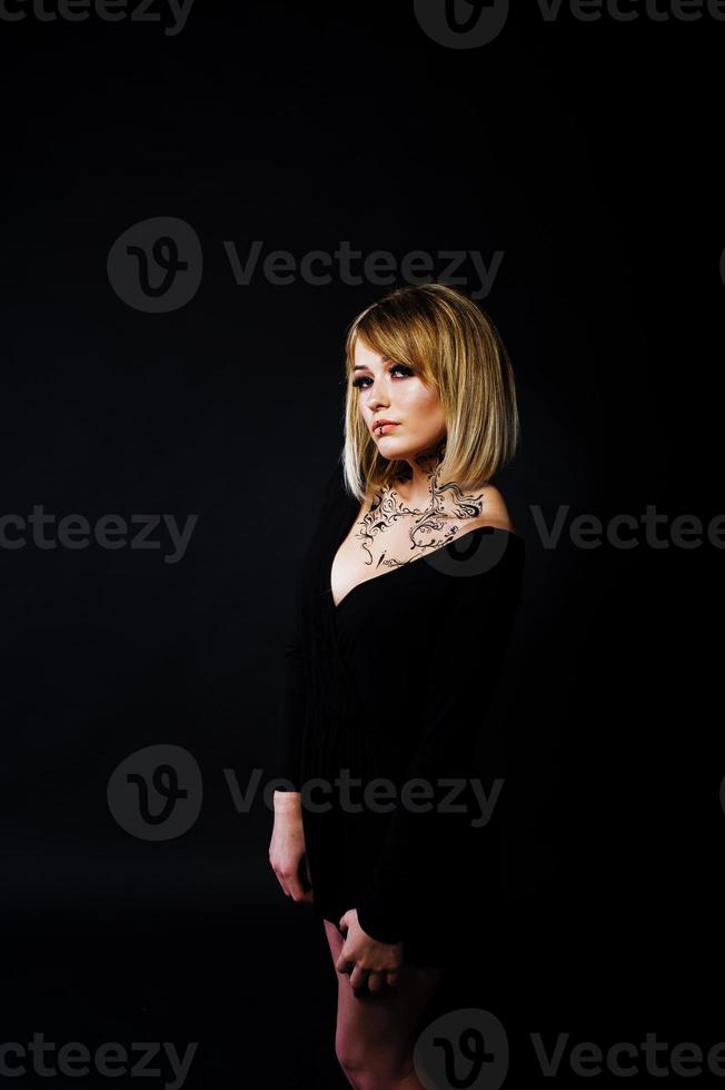 Studio portrait of blonde girl with originally make up on neck, wear on black dress at dark background. photo