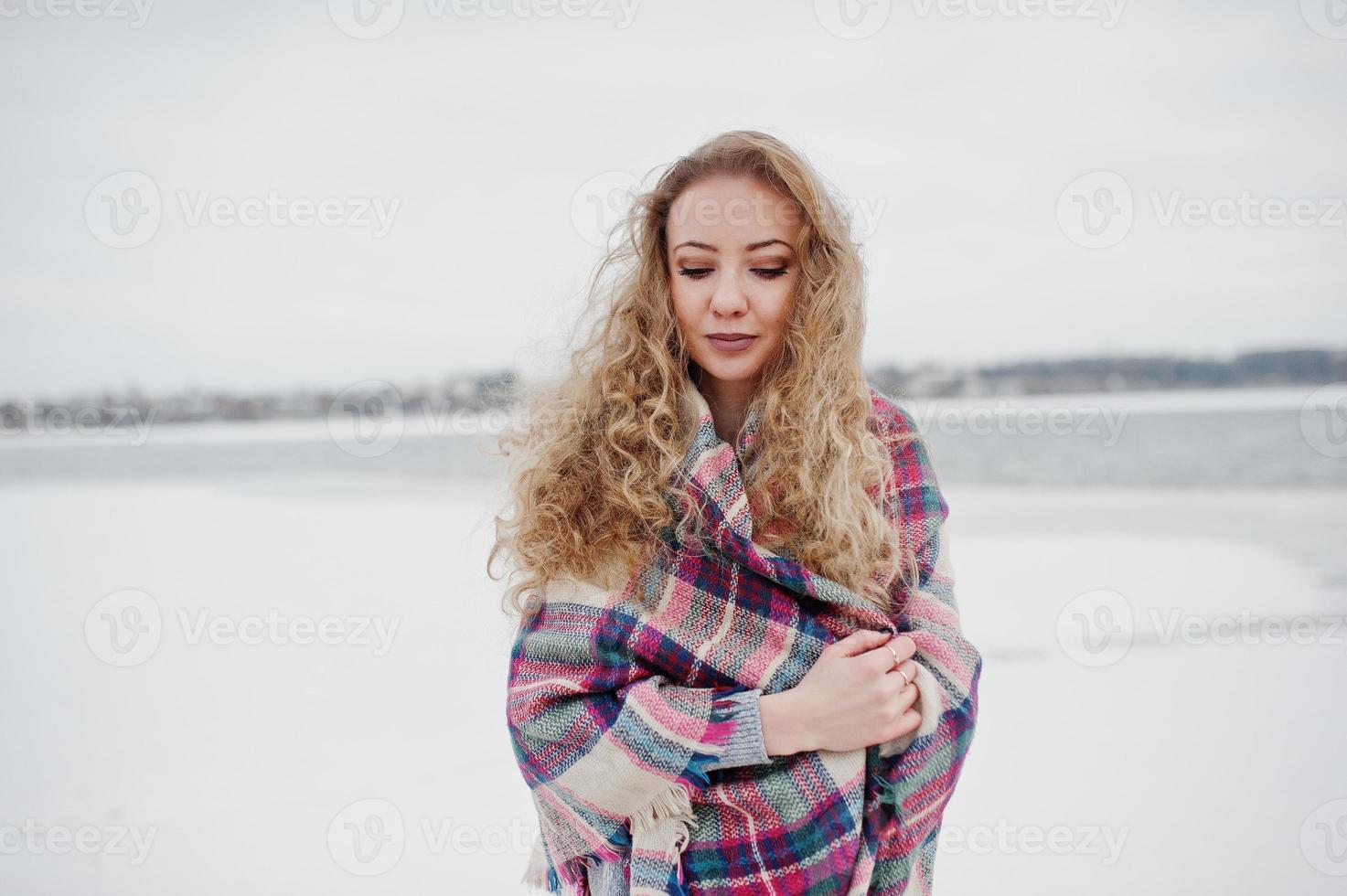 Curly blonde girl in checkered plaid against frozen lake at winter day. photo