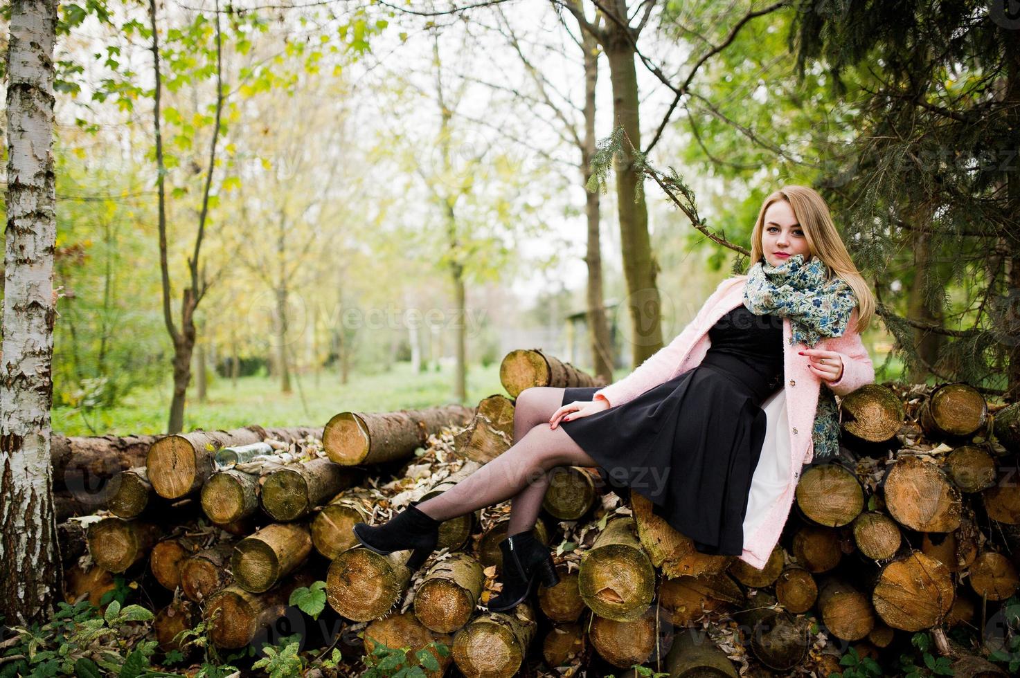 Young blonde girl at pink coat posed against wooden stumps background. photo