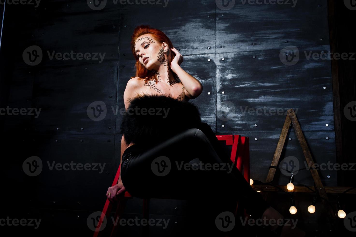 Fashion model red haired girl with originally make up like leopard predator against steel wall. Studio portrait on ladder. photo