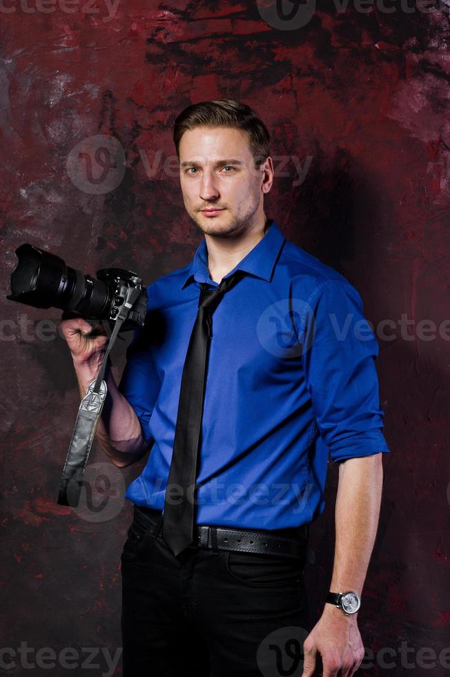 Studio portrait of stylish professional photographer man with camera, wear on blue shirt and necktie. photo