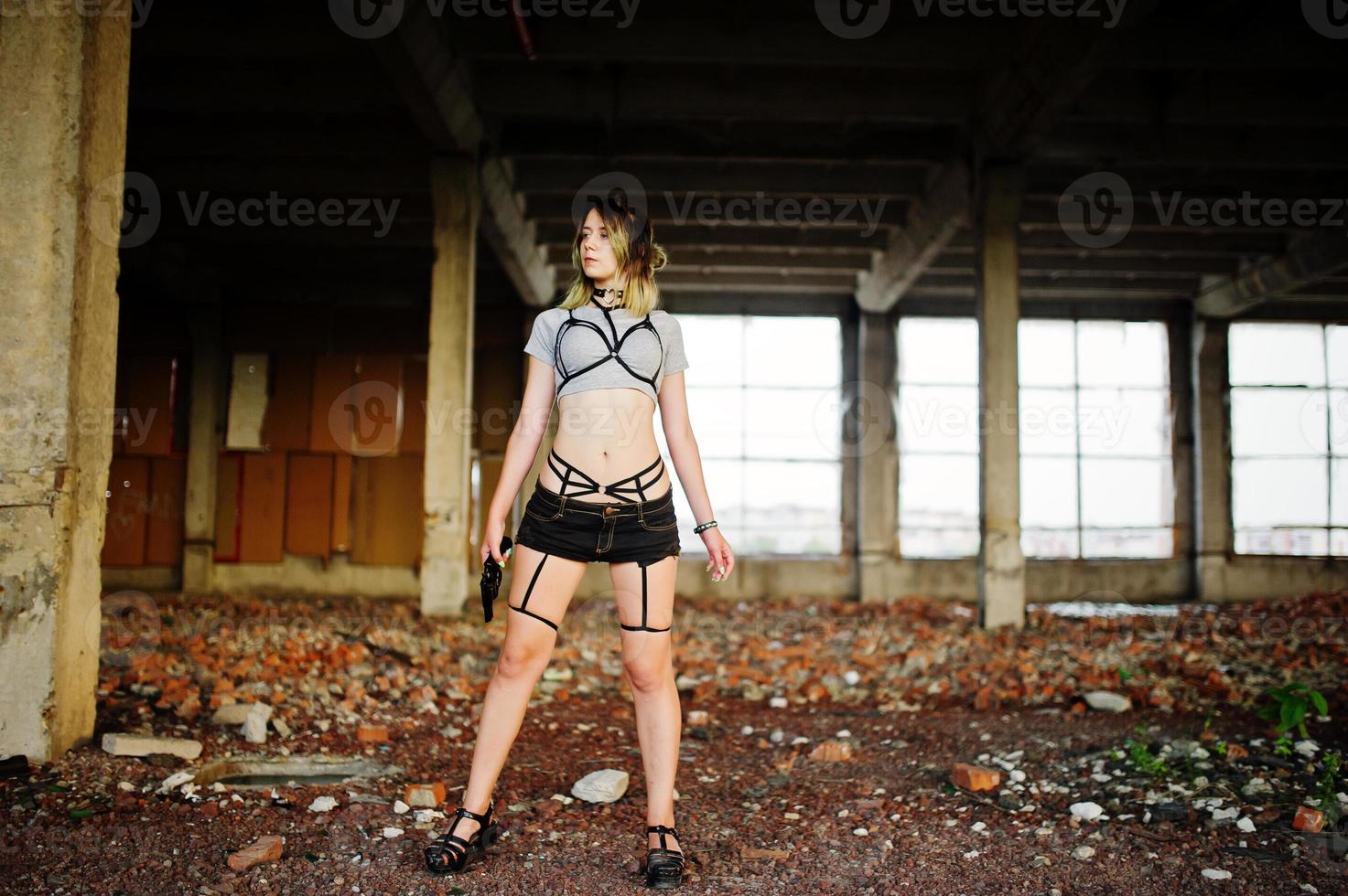 Girl wear on shorts and black erotic fetish underwear with gun at had on abadoned factoty with brick. photo