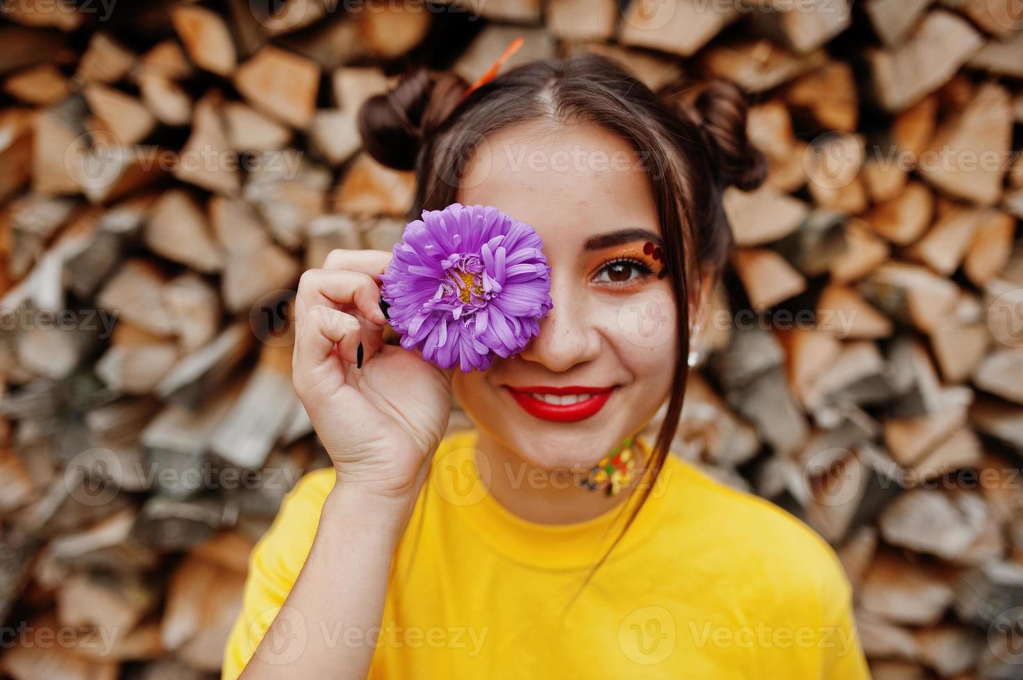 Girl in yellow shirt with violet aster flowers at hand behind eye. photo