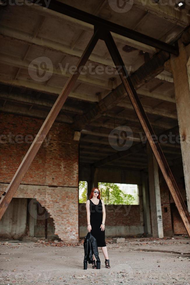 Red haired stylish girl in sunglasses wear in black, against abadoned place. photo