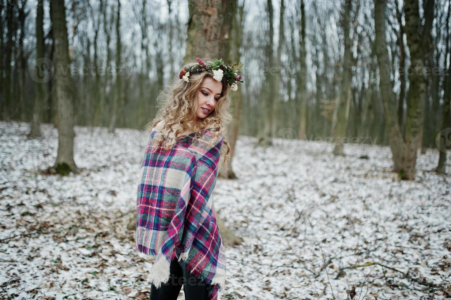 Curly cute blonde girl with wreath in checkered plaid at snowy forest in winter day. photo
