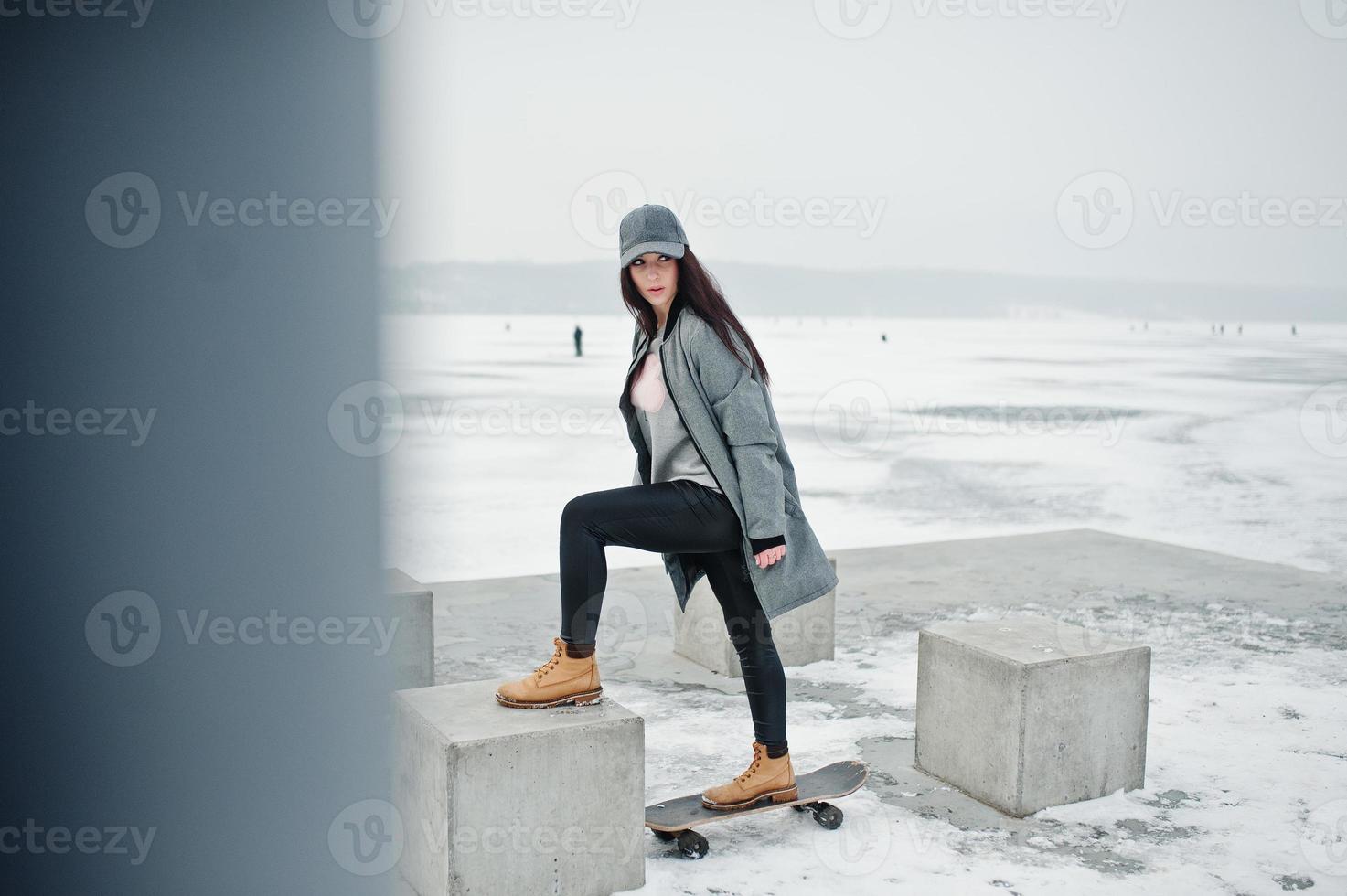 Stylish brunette girl in gray cap, casual street style with skate board on winter day. photo