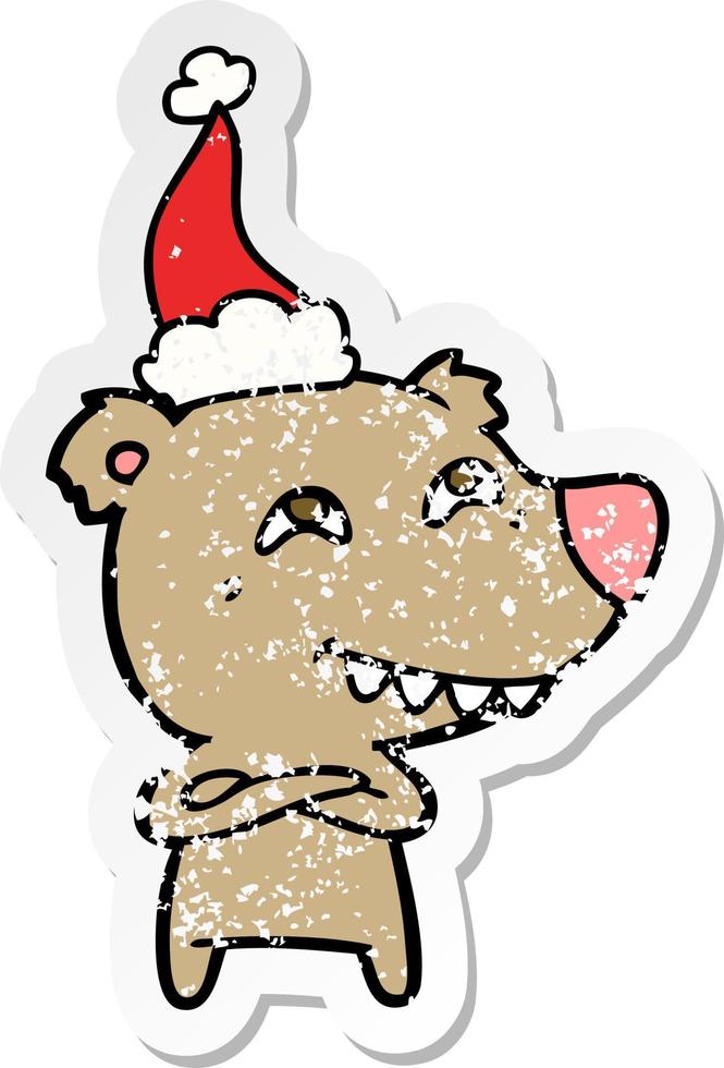 distressed sticker cartoon of a bear showing teeth wearing santa hat vector