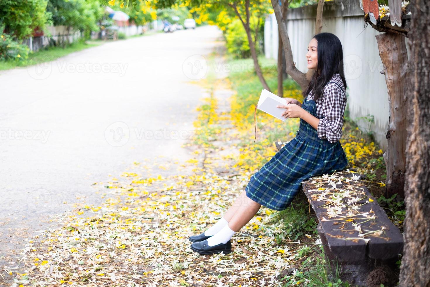 Young girl sitting on a bench reading a book under a beautiful tree. photo