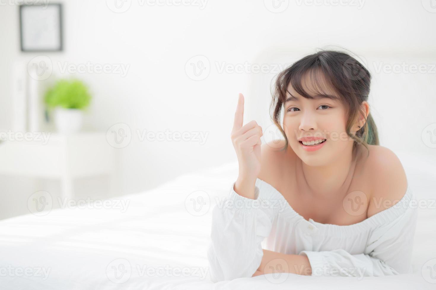 retrato hermosa joven mujer asiática sonrisa despierta saludable y bienestar por la mañana, belleza asia niña acostada y señalando algo cuidado de la piel y maquillaje cosmético con feliz, estilo de vida y concepto de relajación. foto