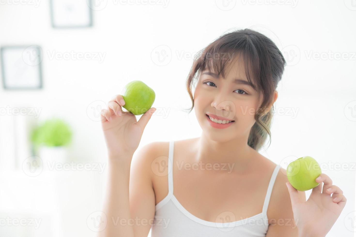 Beautiful portrait young asian woman holding and eating green apple fruit in the bedroom at home, lifestyle of nutrition girl healthy and care weight loss, health and wellness concept. photo