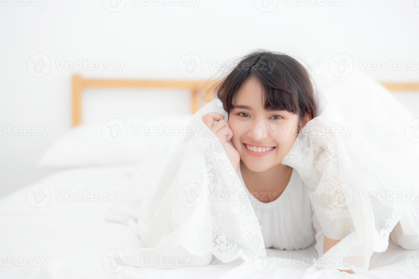 Beautiful portrait young asian woman lying and smile while wake up with sunrise at morning, girl with happy annd fun in the bedroom, lifestyle and relax concept. photo