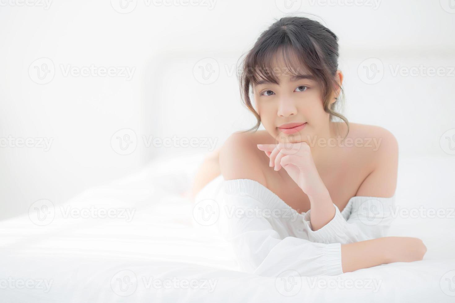 hermoso retrato joven mujer asiática acostada y sonriendo mientras se despierta con el amanecer en la mañana, belleza linda chica feliz y alegre descansando en la cama en el dormitorio, estilo de vida y concepto de relajación. foto