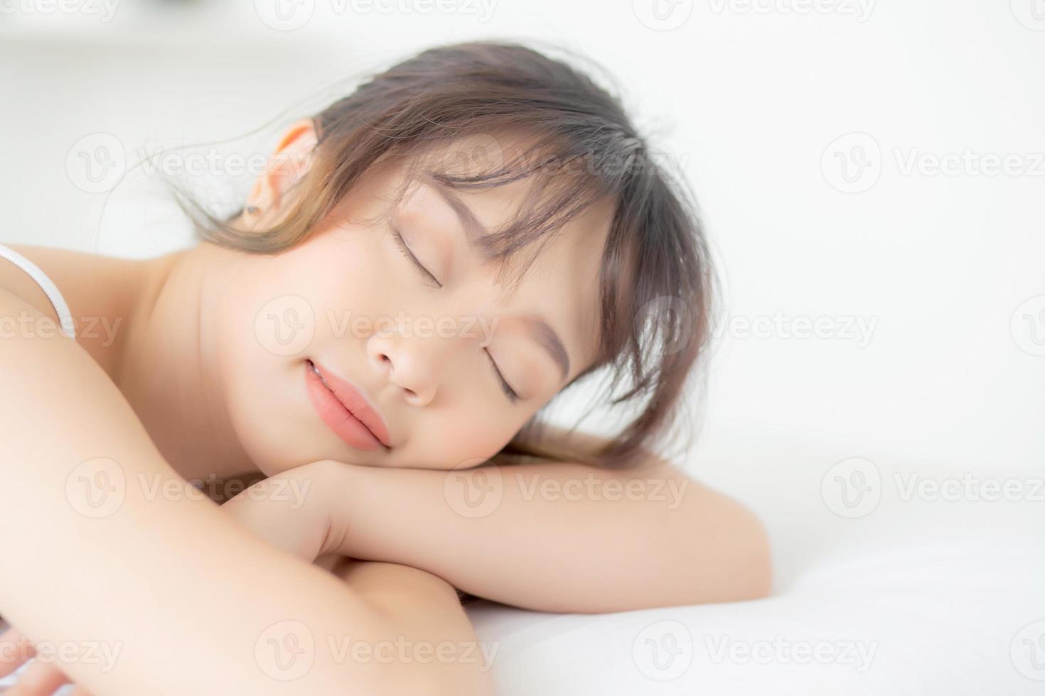 hermosa mujer joven asiática sonríe durmiendo acostada en la cama con un ocio cómodo y feliz en el dormitorio, bienestar de la niña asiática de belleza con relajación y fresco para el concepto de salud. foto