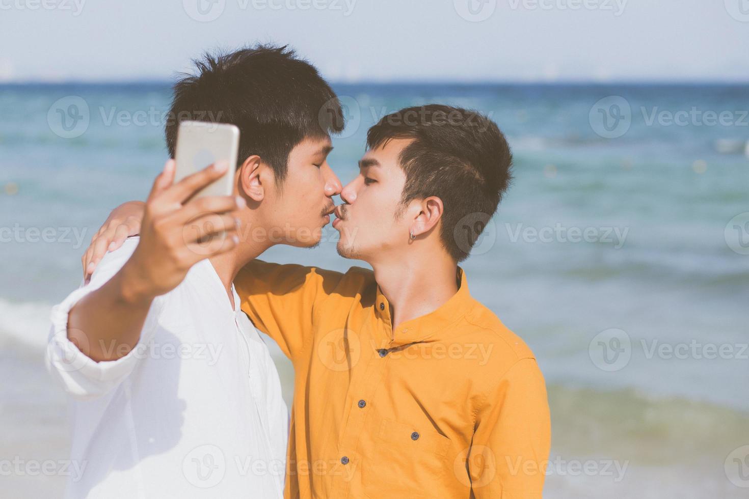 Gay portrait young couple smiling taking a selfie photo together with smart mobile phone at beach, LGBT homosexual lover with kiss in the vacation at sea, two man going to travel, holiday concept.